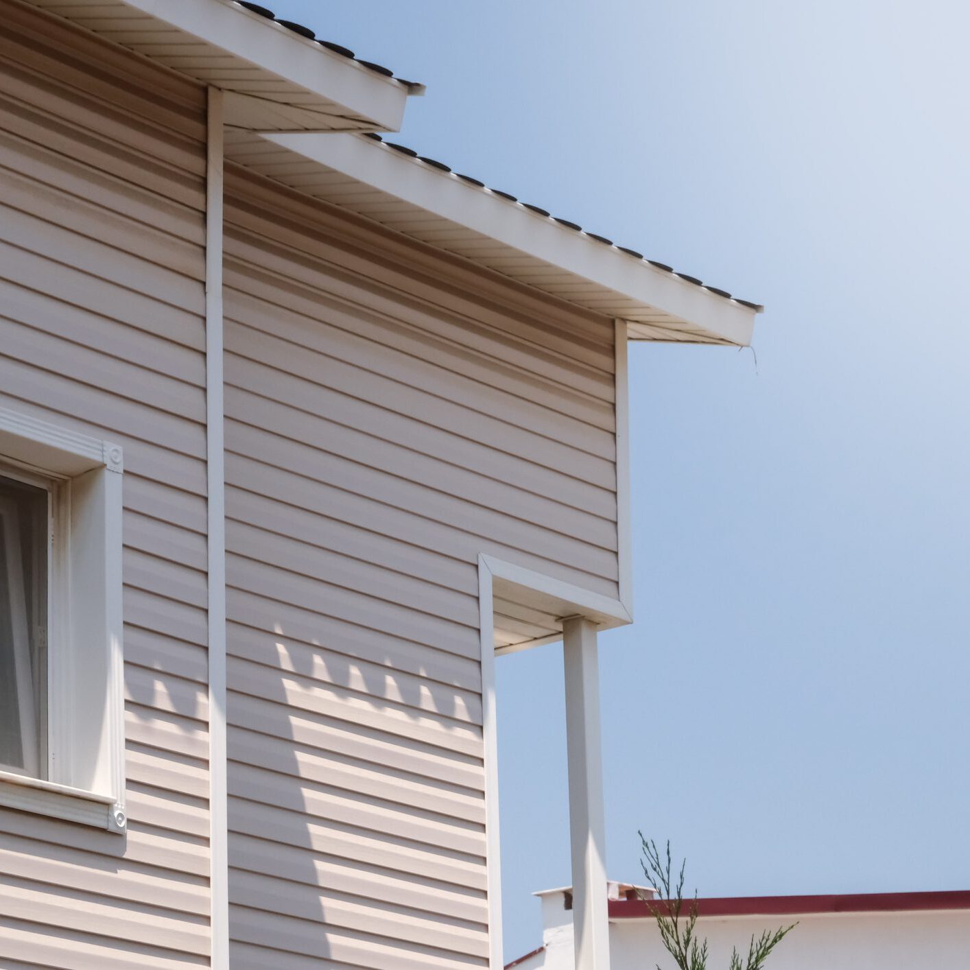 The facade of the new house clad with siding, with windows, against the blue sky.